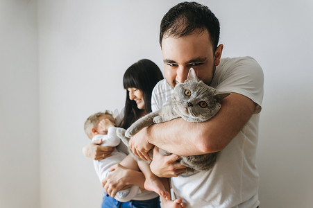 小孩抱着小孩摄影照片_在家里抱着小孩和灰猫的快乐父母的肖像