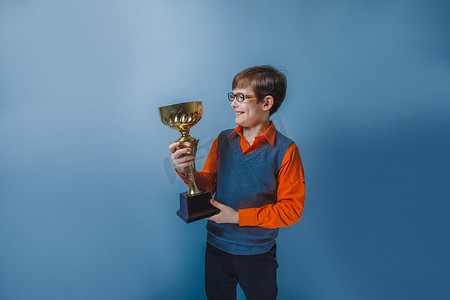主图年中大促摄影照片_欧洲人的小男孩的十年中持有杯奖在蓝色背景上的眼镜