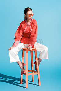 时髦的女人在活珊瑚服装和太阳镜摆在凳子上蓝色