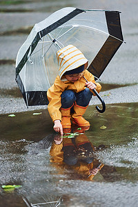 穿着黄色防水斗篷、靴子、雨后带着雨伞在户外玩耍的孩子.