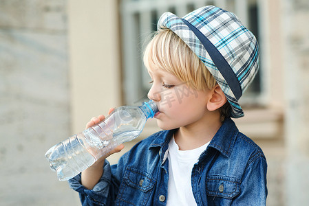 可爱的小男孩从塑料瓶里喝水。孩子们在户外喝水。小孩在街上喝矿泉水健康的童年.