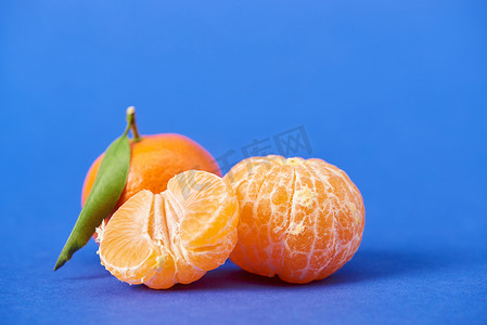橘子去皮摄影照片_一半去皮的橘子在蓝色背景的整体克莱门汀附近 