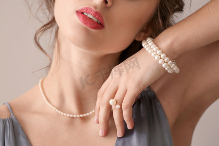 年轻的女人与美丽的珍珠首饰在轻的背景, 特写镜头