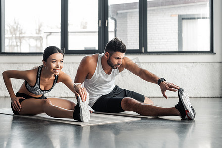 运动的年轻男女在健身房的瑜伽垫上伸展双腿