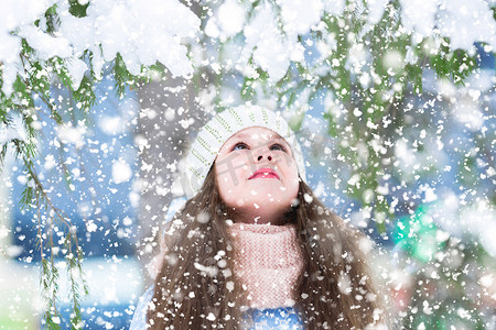 圣诞祝福摄影照片_冬天森林里的小女孩用雪抬头望着冷杉的树枝。等待奇迹, 许下圣诞祝福.