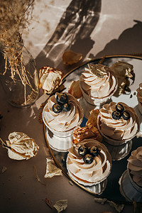 dried摄影照片_Set of cupcakes on a round mirror, sunset light, dried flowers, beige composition