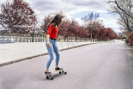 玩滑板的女子摄影照片_在公园用长板练习滑板的很酷的女子，玩得很开心.