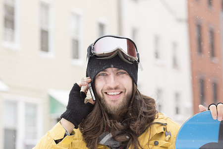 年轻人手持滑雪板在街上用智能手机聊天的肖像