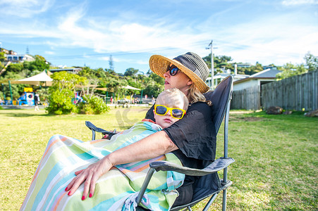 新西兰文化摄影照片_在新西兰怀赫克岛的帕克一个戴着黄色太阳镜的男孩坐在母亲的腿上