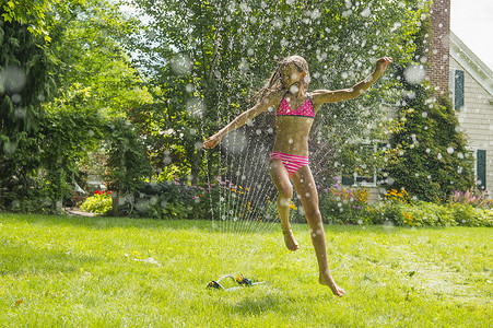 穿着泳装的女孩跳过花园洒水器