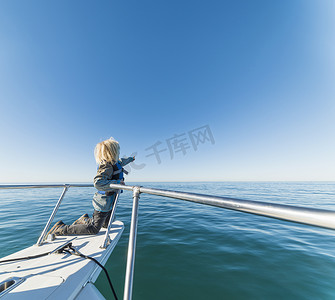 男孩跪在帆船的船头看着别处指着