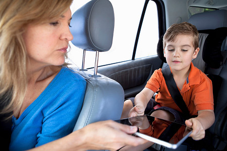 坐在汽车后座上的母亲把平板电脑递给儿子