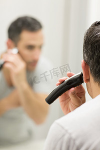 剃须刀片摄影照片_中年男子照镜子使用电动剃须刀后视镜