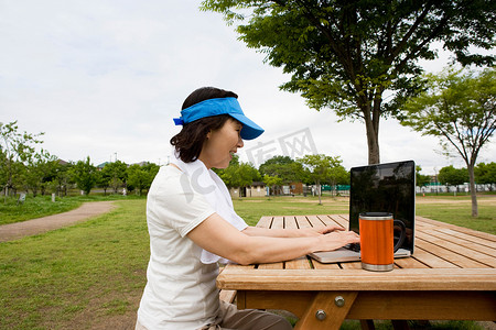 一名女子在公园的野餐长凳上使用笔记本电脑