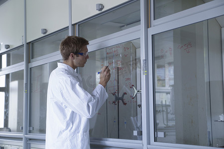 化学思考摄影照片_年轻的男科学家在通风柜窗户上写结果
