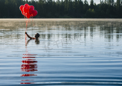 装饰漂浮图案摄影照片_水中女子手持一串红色气球