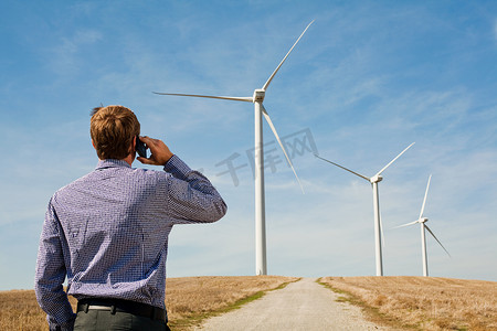 电视与网络摄影照片_一名男子在手机上看风力涡轮机