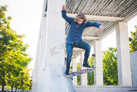 运动休闲裤子摄影照片_城市年轻男子滑板运动员滑下混凝土结构