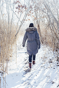 身着冬衣的女子在雪地上行走的全身后视