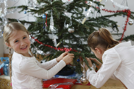 友谊装饰摄影照片_女孩们用金属片装饰圣诞树回头看着镜头微笑