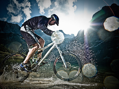 游戏光线摄影照片_男子山地自行车运动员在水中骑行