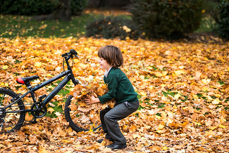 公园里的男孩骑着自行车在秋叶里玩耍