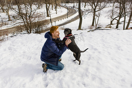 一名年轻男子在白雪皑皑的中央公园抚摸小狗纽约美国