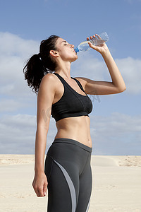 中年妇女在海滩上锻炼时用水瓶喝水