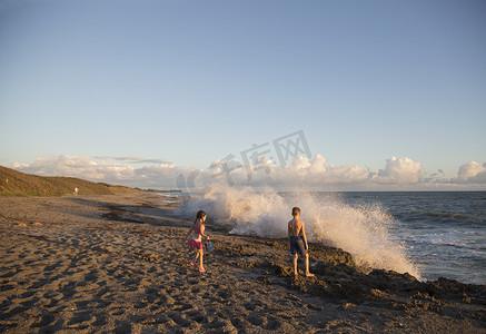 石凯摄影照片_男孩和妹妹在美国佛罗里达州朱庇特岛的海滩上看着溅起的海浪吹石保护区