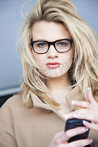 戴眼镜拿着智能手机的金发年轻女子肖像