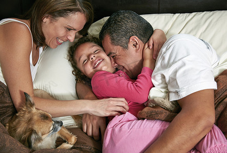 女孩与父母和狗在床上的高空视角拥抱挠痒微笑