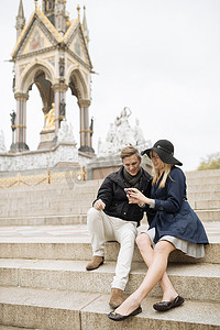 迈特凯摄影照片_一对年轻夫妇坐在台阶上阅读智能手机短信阿尔伯特纪念堂英国伦敦