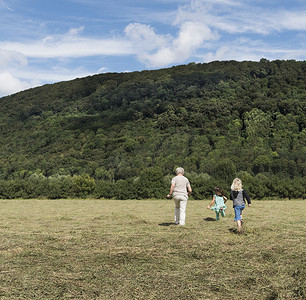 德国北莱茵威斯特伐利亚州韦斯特法利卡门祖母和孙子孙女慢跑穿过田野的背影