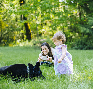 一名女子在公园拍摄蹒跚学步的女儿和拉布拉多犬