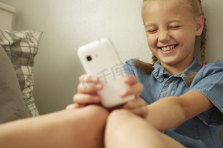 女孩靠墙坐着手持智能手机闭着眼睛微笑