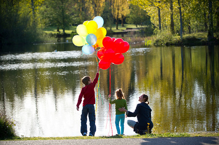 母亲和孩子们手持一串串气球站在湖边