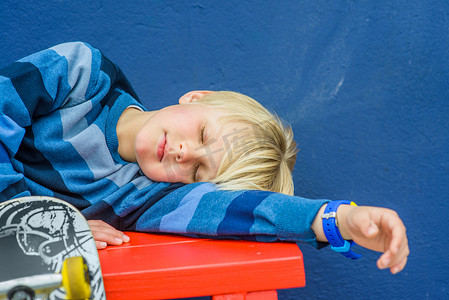 穿着滑板睡在红板凳上的男孩