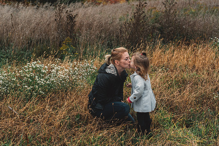 一名中年妇女在草地上亲吻蹒跚学步的女儿