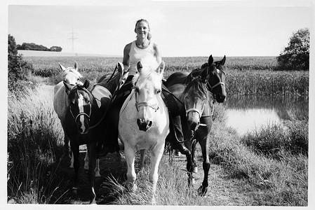 黑白图像女子骑马牵着六匹马走在土路上
