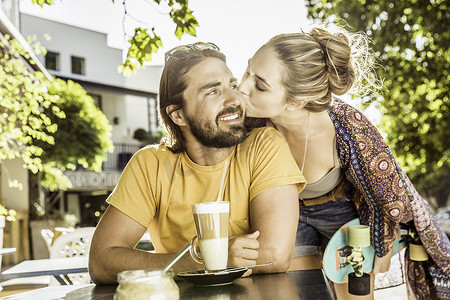 路边咖啡厅摄影照片_年轻女子在路边咖啡馆亲吻男友的脸颊南非