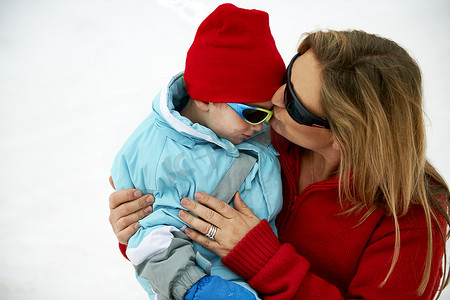 滑雪妈妈亲吻蹒跚学步的儿子额头