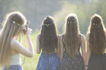 十几岁的女孩在公园里给戴着雏菊链条头饰的朋友拍照的背影