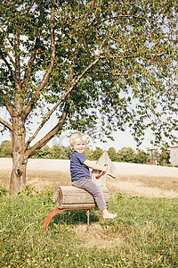 追逐摄影照片_德国巴登符腾堡州乌尔姆男孩坐在树旁的木马上微笑着看着相机的侧视