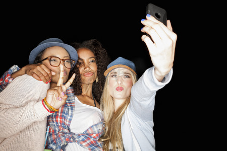 年轻女性挤在一起做和平手势眯着嘴唇用智能手机自拍