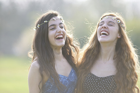 两个戴着菊花链头饰的十几岁女孩在公园里笑
