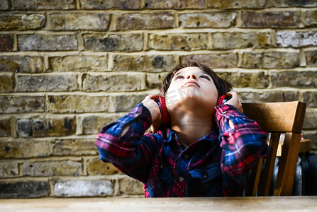 坐在桌子旁的男孩一边听着耳机一边抬头凝视