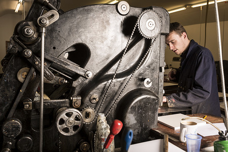 年轻的男印刷工在印刷机车间操作印刷机械