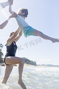 新西兰群岛湾热水海滩两名妇女将女孩举过海浪