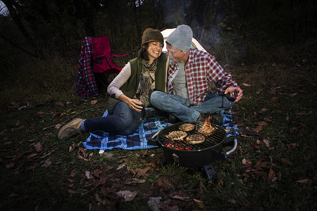 一对成熟的夫妇坐在帐篷外端着烧烤和一杯葡萄酒