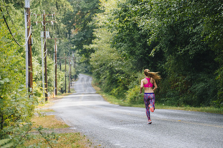十几岁的女跑步者在乡村公路上奔跑的背影